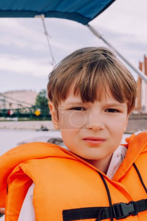 Téléchargez les photos : Enfant assis dans un bateau en veste de sécurité - en image libre de droit