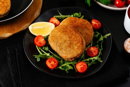 Téléchargez les photos : Escalopes de poulet sur une assiette noire. légumes et herbes. fond noir - en image libre de droit