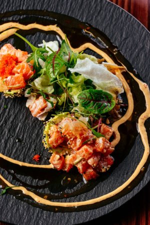 Photo for Salmon tartare with sauce and herbs on a black plate - Royalty Free Image