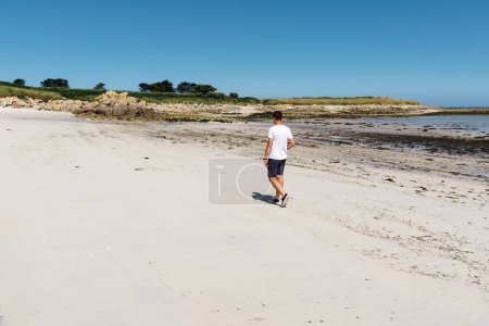 Téléchargez les photos : Portrait complet d'un jeune homme séduisant marchant le long de la plage - en image libre de droit