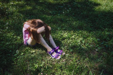 Foto de Girl sitting on the grass hiding her face - Imagen libre de derechos