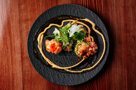 Téléchargez les photos : Tartare de saumon avec sauce et herbes sur une assiette noire - en image libre de droit