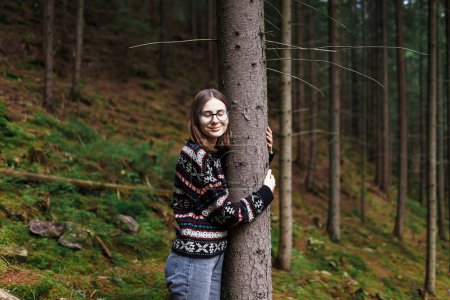 Téléchargez les photos : Femme jouissant de la nature dans la forêt embrassant un tronc d'arbre en silence seul - en image libre de droit