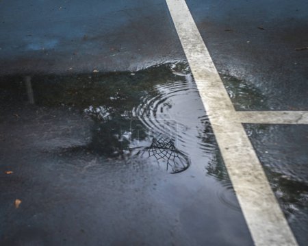 Téléchargez les photos : Reflet du but de basket-ball dans la flaque d'eau un jour de pluie - en image libre de droit