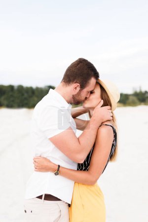 man and a woman are kissing and hugging on a sandy beach