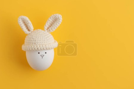 Photo for Easter egg in crochet hat with bunny ears on yellow background. Flat lay. Horizontal banner, post card - Royalty Free Image