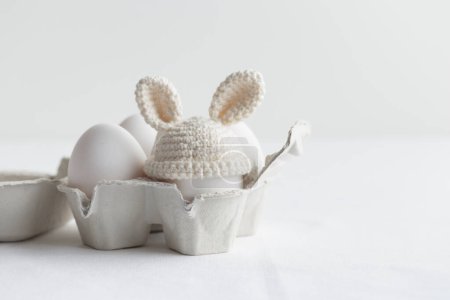 Photo for Easter egg in crochet hat with bunny ears in the eggbox on white background. Horizontal banner, post card with copyspace - Royalty Free Image