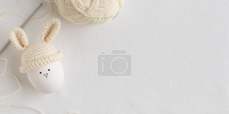 Foto de Huevo de Pascua en sombrero de ganchillo con orejas de conejo sobre fondo blanco. Acostado. Banner horizontal, tarjeta postal - Imagen libre de derechos