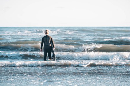 Photo for Tween boy wearing a wetsuit and holding a surfboard at the beach - Royalty Free Image