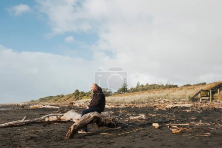 Téléchargez les photos : Homme assis sur du bois flotté regardant l'océan - en image libre de droit