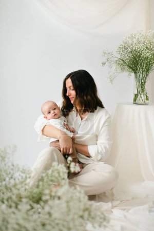 Photo for Sitting young mother holding newborn baby son by baby's breath flowers - Royalty Free Image