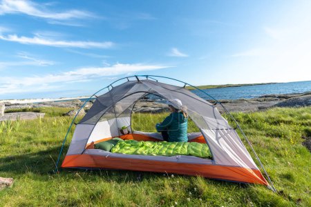 Téléchargez les photos : Voyageur assis dans sa tente, admirant le paysage sur la plage - en image libre de droit