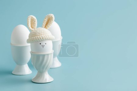 Foto de Huevo de Pascua en sombrero de ganchillo con orejas de conejo sobre fondo azul. Banner horizontal, tarjeta postal con copyspace - Imagen libre de derechos