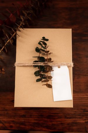 Foto de Etiqueta de regalo blanca en blanco con caja de regalo marrón, cordel, hojas de eucalipto - Imagen libre de derechos