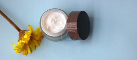 Photo for Jar of moisturizer for the face next to a yellow flower. - Royalty Free Image