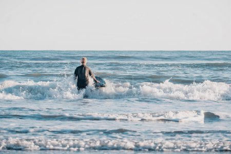 Téléchargez les photos : Entre garçon en combinaison tenant une planche de surf dans l'eau - en image libre de droit