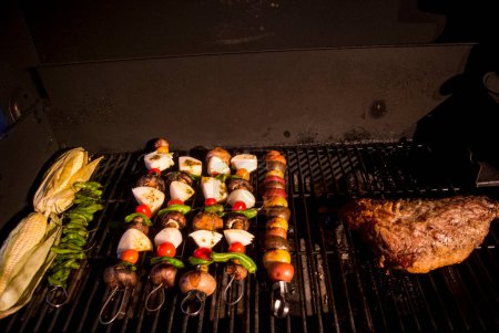 Téléchargez les photos : Maïs et kabobs et un steak géant à trois pointes cuisiner sur un barbecue la nuit. - en image libre de droit