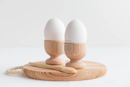 Photo for White eggs in a wooden egg holders standing on a white table. Horizontal banner, post card, easter - Royalty Free Image