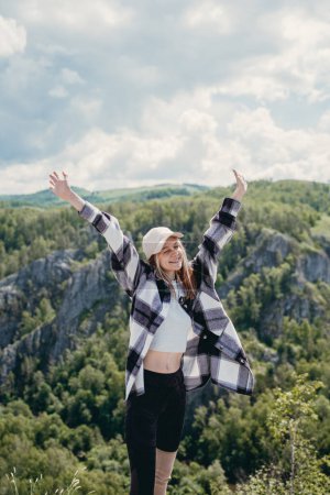 Photo for A girl in a checkered shirt raised her hands high in the mountains - Royalty Free Image