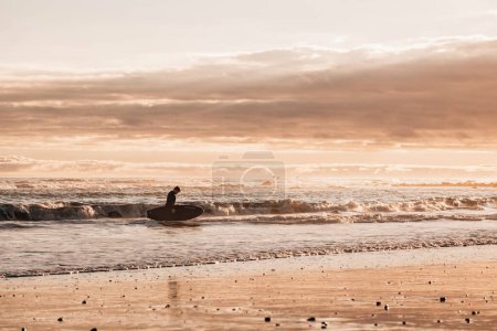 Photo for Tween boy with a surfboard in the water during sunset - Royalty Free Image