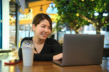 Photo for Asian woman sitting at a table in a restaurant and working with - Royalty Free Image