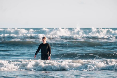 Photo for Tween boy wearing a wetsuit walking out of the waves at the beach - Royalty Free Image