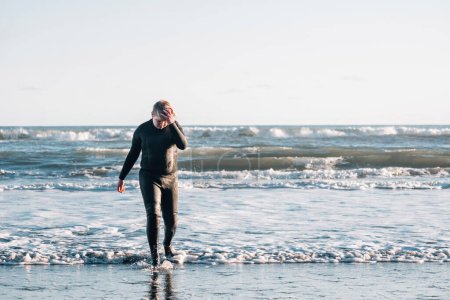 Téléchargez les photos : Entre garçon dans une combinaison de plongée marchant sur la terre de plage regardant vers le bas - en image libre de droit