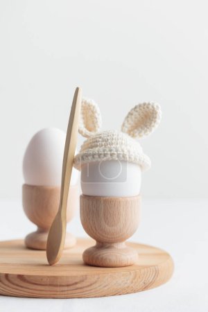 Photo for Easter egg in crochet hat with bunny ears in wooden egg holder on white background. Vertical banner, post card with copyspace - Royalty Free Image