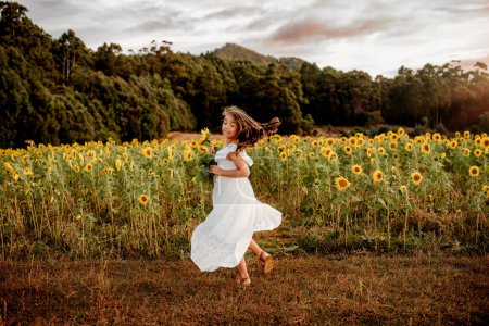 Foto de Chica joven en vestido blanco fluido bailando en el campo de los girasoles - Imagen libre de derechos