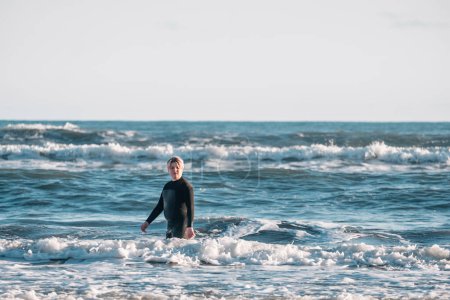 Foto de Tween chico usando un traje de neopreno de pie en el agua en la playa - Imagen libre de derechos
