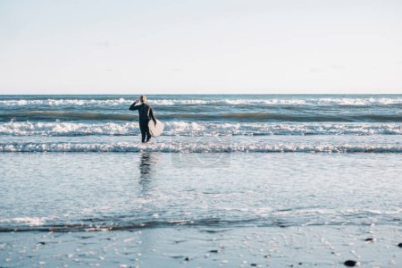 Photo for Tween boy wearing a wetsuit and holding a surfboard in the water - Royalty Free Image