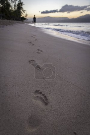 Téléchargez les photos : Pas dans le sable au coucher du soleil avec marcheur au loin - en image libre de droit