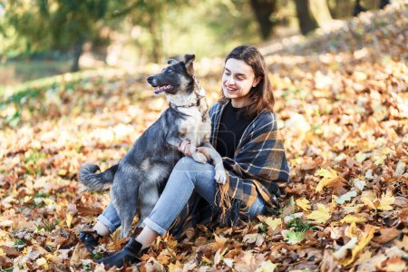 Foto de Mujer joven pasea a su perro en un parque de otoño lleno de hojas - Imagen libre de derechos