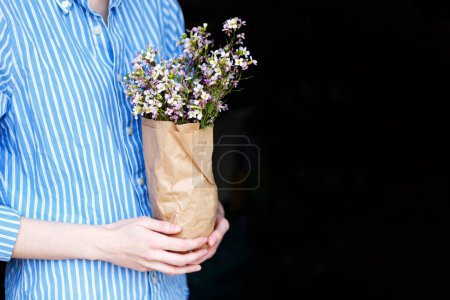 Photo for Woman in blue shirt holds package of flowers in her hands at home - Royalty Free Image