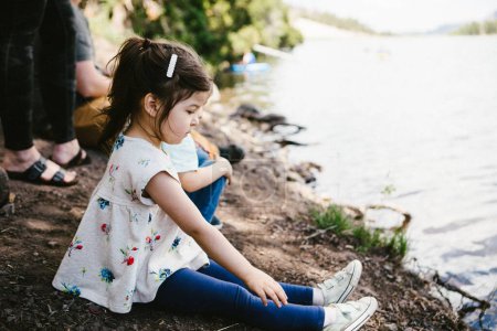 Téléchargez les photos : Petite fille portant une robe et s'installant sur le bord du lac en famille - en image libre de droit
