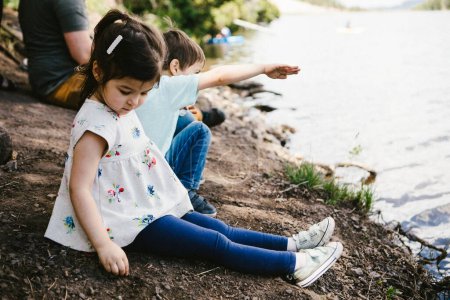 Téléchargez les photos : Petite fille et garçon s'amuser sur la rive d'un lac en famille - en image libre de droit