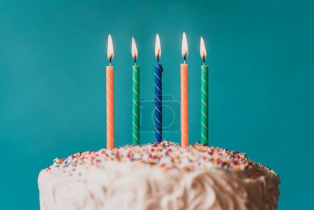 Photo for Lit candles on top of a birthday cake against blue background. - Royalty Free Image