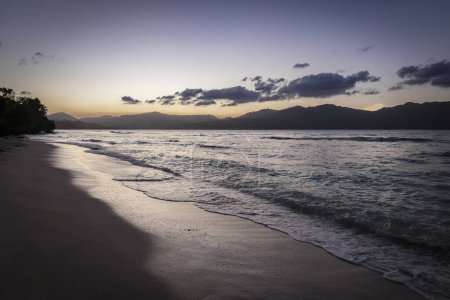 Téléchargez les photos : Plage des Caraïbes et vagues au coucher du soleil avec des montagnes au loin - en image libre de droit