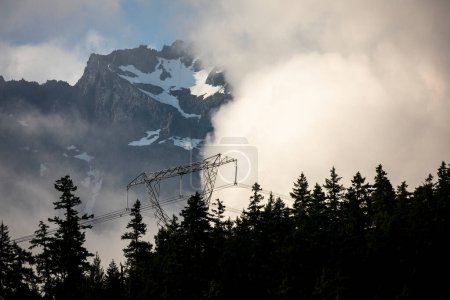 Foto de Contraste entre las líneas eléctricas de alto voltaje y los picos de montaña cubiertos de nieve detrás. - Imagen libre de derechos