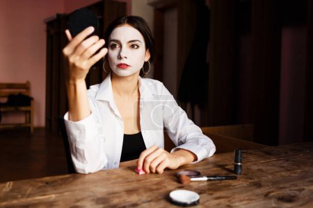 Téléchargez les photos : Actrice applique maquillage sur son visage tout en étant assis au théâtre de répétition - en image libre de droit