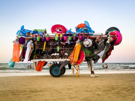Foto de Vendedor tirando de un coche de venta de recuerdos sobre la playa. - Imagen libre de derechos