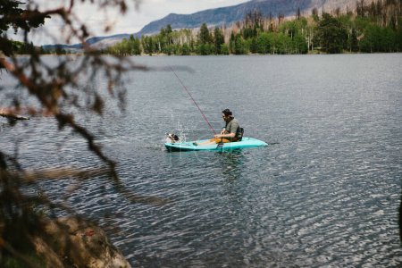 Téléchargez les photos : Homme pêchant en kayak sur un lac en montagne avec chien - en image libre de droit