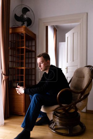 Foto de Hombre en un suéter negro y vaqueros azules solo en su apartamento - Imagen libre de derechos