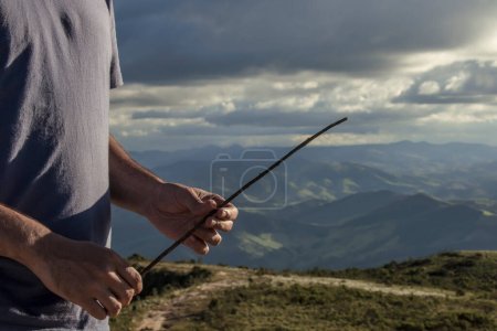 Foto de Hombre sosteniendo una rama en el paisaje salvaje de montañas verdes - Imagen libre de derechos