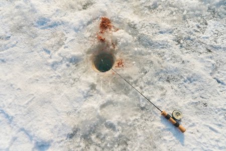 Foto de La caña de pescar se encuentra en la nieve junto al agujero, vista superior - Imagen libre de derechos