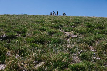 Téléchargez les photos : Des gens sur une colline herbeuse regardant le ciel bleu en randonnée - en image libre de droit