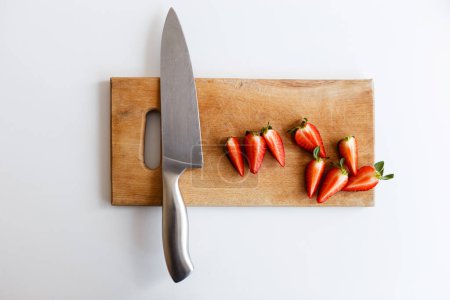 Foto de Cuchillo con fresas se encuentra en una tabla de cortar de madera en la cocina - Imagen libre de derechos