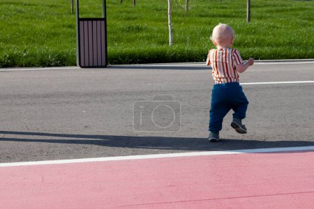 Téléchargez les photos : Petit garçon marchant sur la route asphaltée dans la vue sur le parc de dos - en image libre de droit