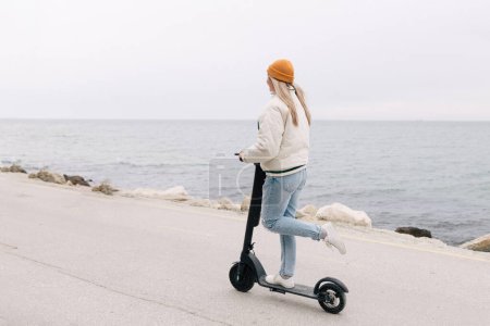 Foto de Chica atractiva montando un scooter eléctrico a lo largo del paseo marítimo - Imagen libre de derechos
