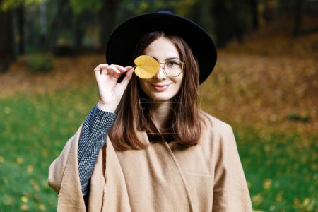 Téléchargez les photos : Femme aux cheveux bruns dans un chapeau noir et poncho marche dans le parc d'automne - en image libre de droit